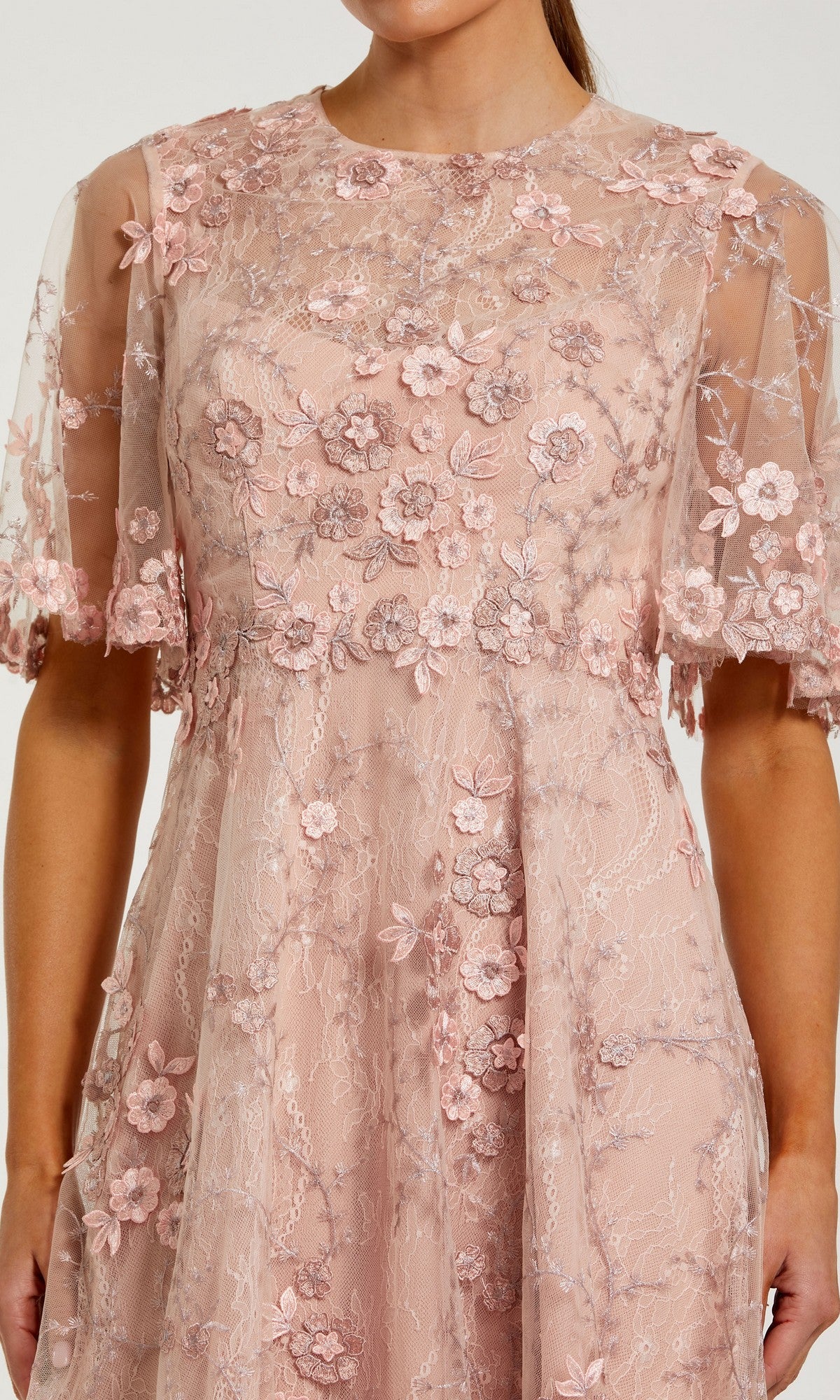 A woman wears the Midi Wedding Guest Dress: Mac Duggal 69036 in light pink, featuring floral lace embroidery and a sheer overlay on the bodice and sleeves.